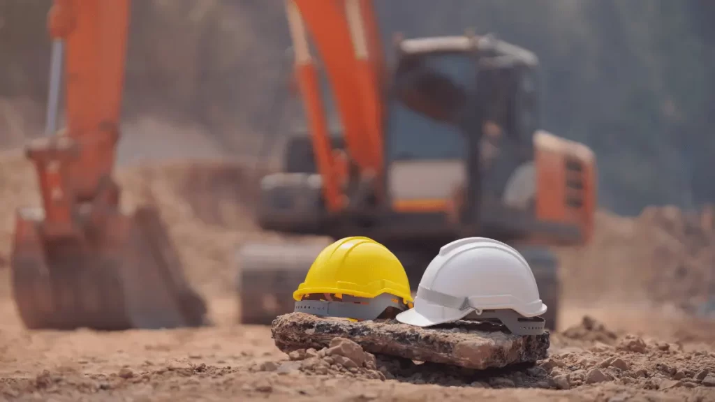 due caschi da lavoro con sullo sfondo una ruspa
