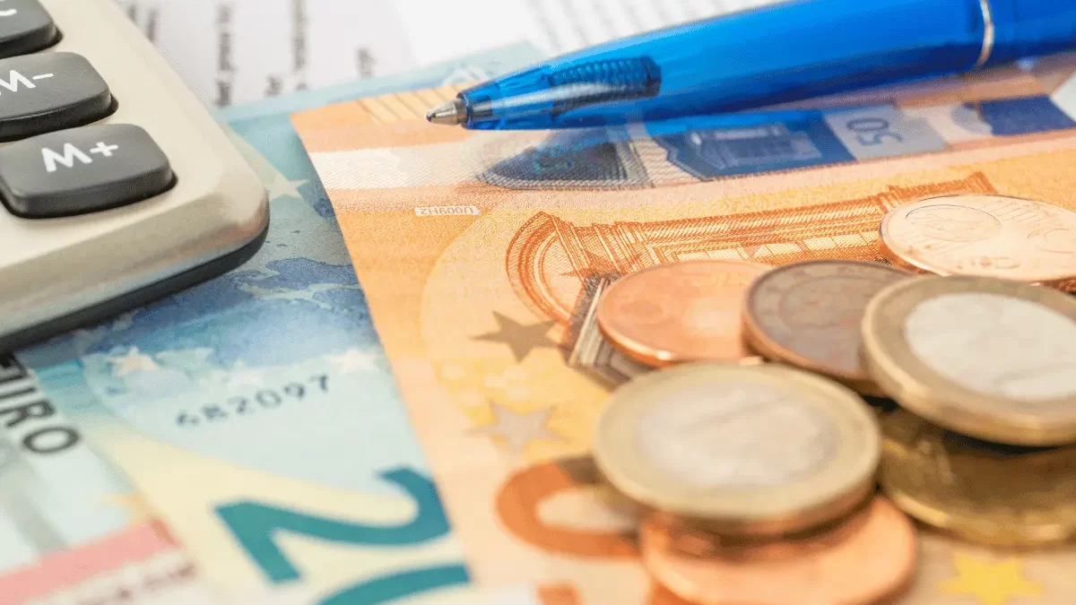 banconote e monete vicino ad una penna e ad una calcolatrice